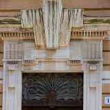 ...con una trabeazione di stampo neoclassico con triglifi e cornice a dentelli spezzata da un massiccio elemento centrale